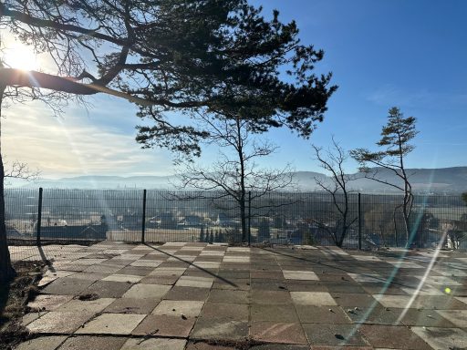 Aussichtspunkt mit Bäumen, Fußwegen und weitem Blick auf eine sonnige Landschaft.