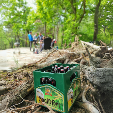 Kasten mit Flaschen Bier im Vordergrund, im Hintergrund Menschen in der Natur.