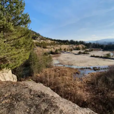 Landschaft mit Fluss, Bäumen und Hügeln unter klarem Himmel.